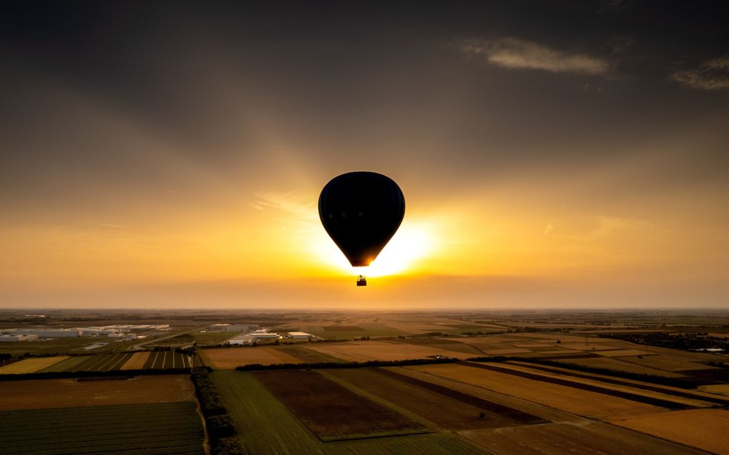 Zonsondergang boven vlakke velden, voor de zon hangt een luchtballon