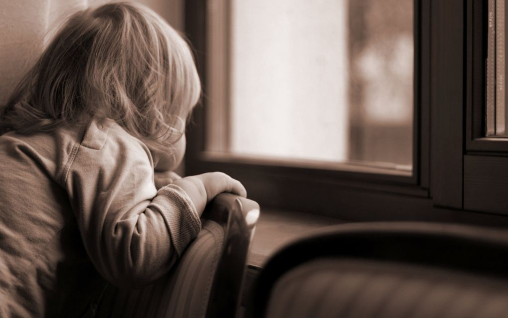 Sepiafoto van een blond kind dat over de leuning van een stoel door een raam staart.