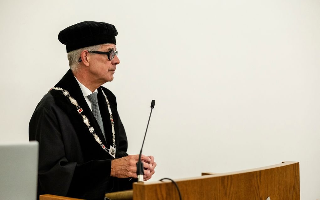 Man in zwarte toga, met zwarte baret, houdt voordracht.