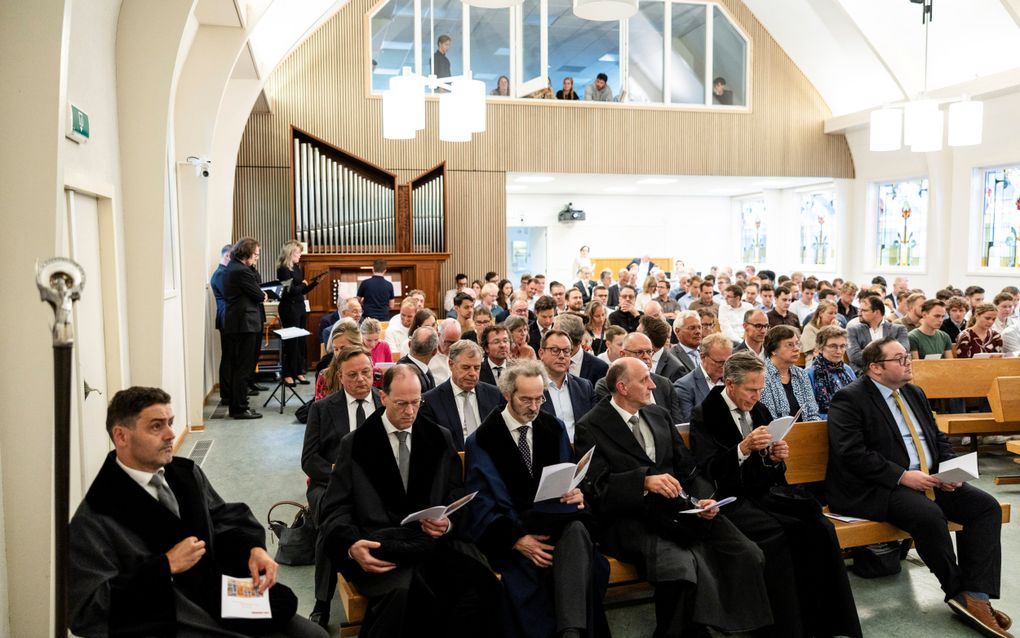 Een zaal vol mensen, gezeten op kerkbanken. Voorin een rij mannen in zwarte toga’s. Achterin een pijporgel en een klein kamerkoor.