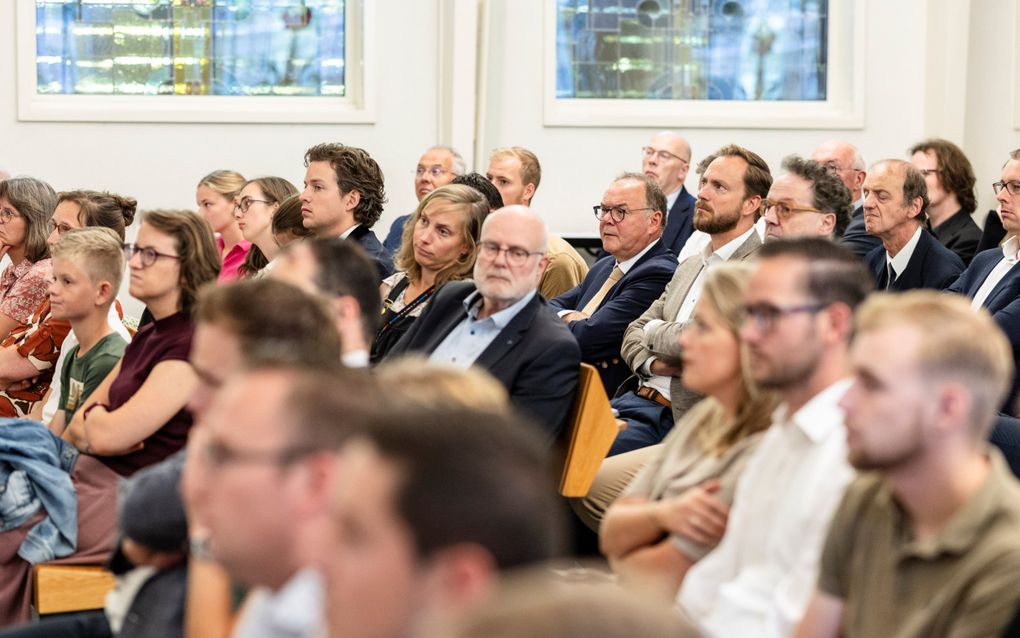 Luisterende gezichten, van jonge mannen en vrouwen, in de zaal van een aula.