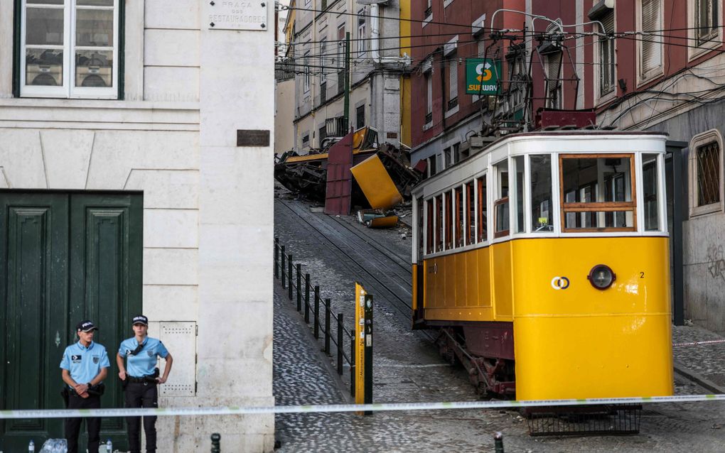 Politieagenten staan naast een afgesloten omhooglopende straat. Op de voorgrond een gele tram, op de achtergrond een totaal verwoeste tram. 