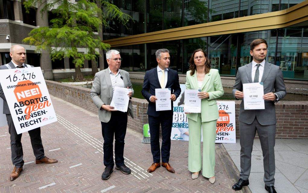 Vijf mensen staan buiten voor het gebouw van de Kamer. Een van hen heeft een bord met een tekst voor zijn buik, de andere vier hebben een document in hun handen.