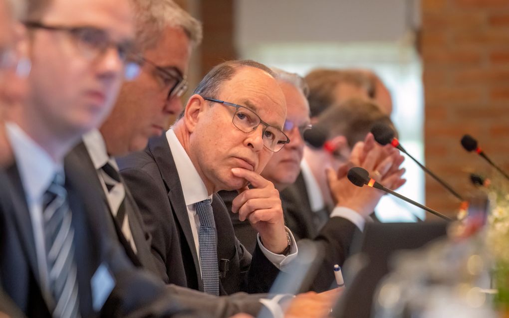 Dominee Buijs, een man met bril, tussen andere mannen achter microfoons.