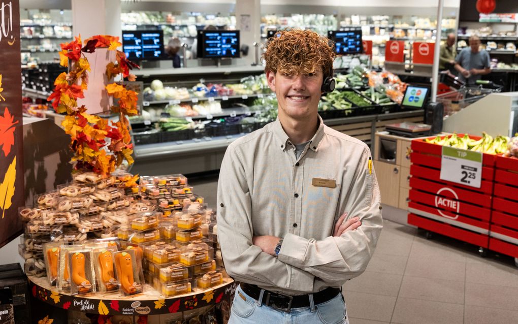 Kevin van Os, jonge vent met donkerblond krulhaar, staat met de armen over elkaar in een supermarkt, met op de achtergrond de koelvitrine en bakken met groenten en fruit