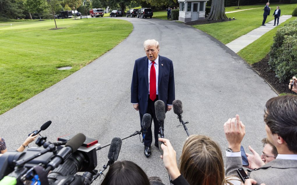 President Trump staat midden op een weg en spreekt met journalisten.