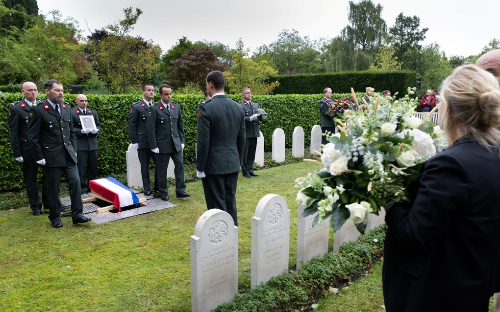 Militairen op een begraafplaats met allemaal dezelfde zerken, naast een graf waarop ze kistje hebben geplaatst met daarop een vlag.