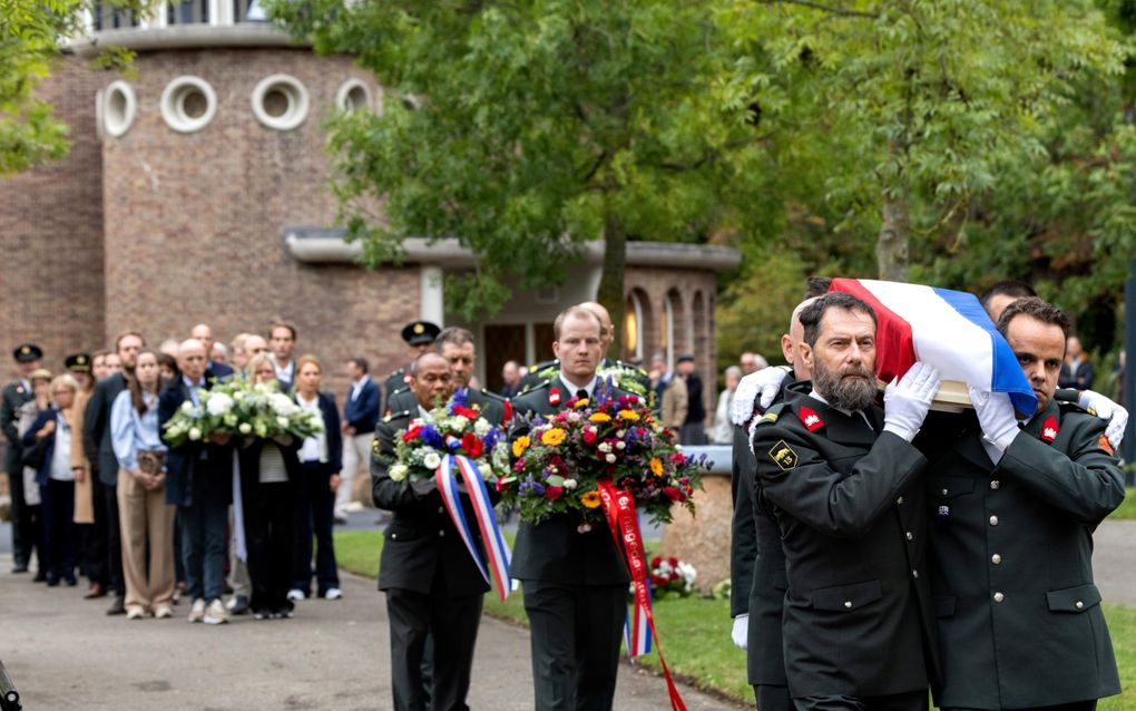 Stoet met de kist en bloemstukken verlaat de aula.