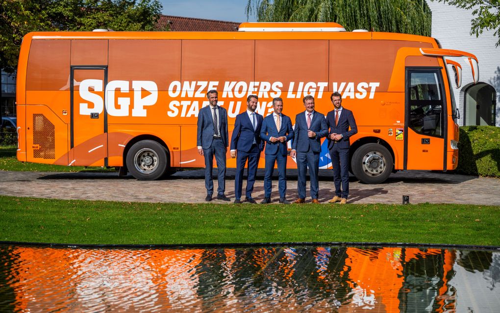 Vijf mannen staan voor een oranje campagnebus van de SGP.