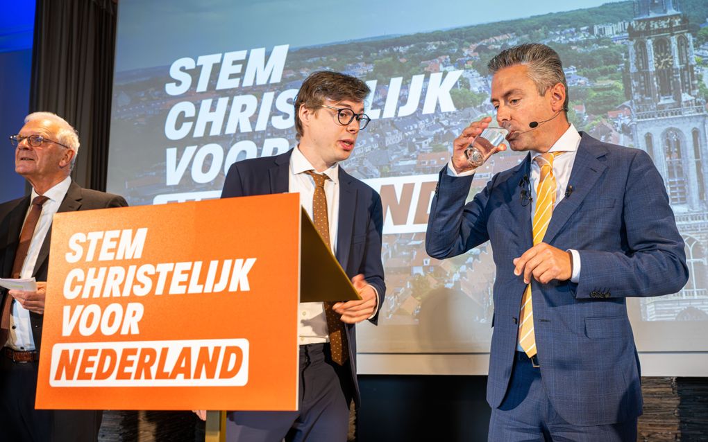 Mannen in pak bij een slogan van de SGP op een spreekgestoelte.