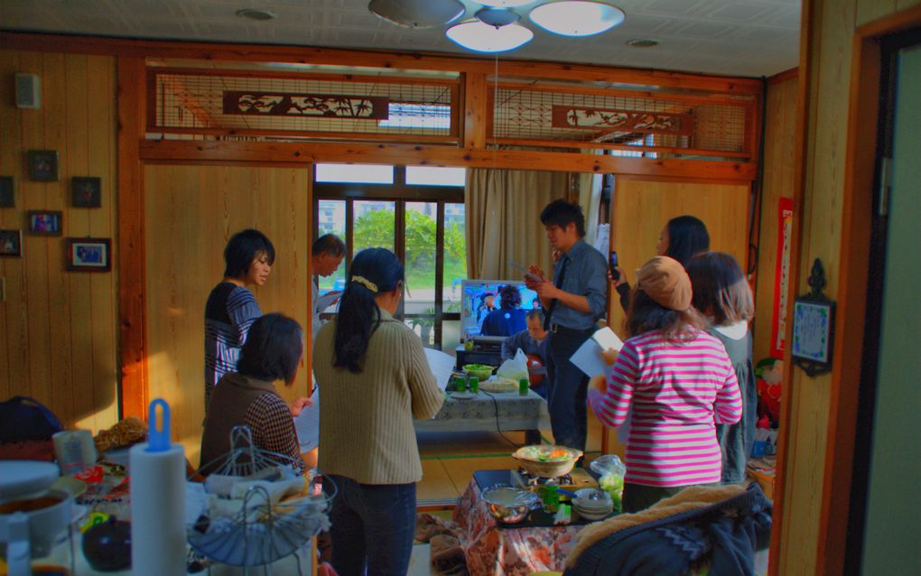 Groep Chinezen in een huiskamer, ze staan in een kring en lezen in een Bijbel.