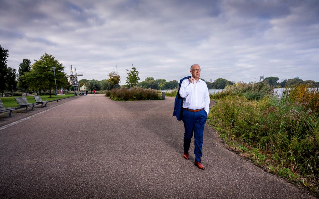 Man loopt langs het water. Hij draagt zijn colbertjasje over zijn schouder.