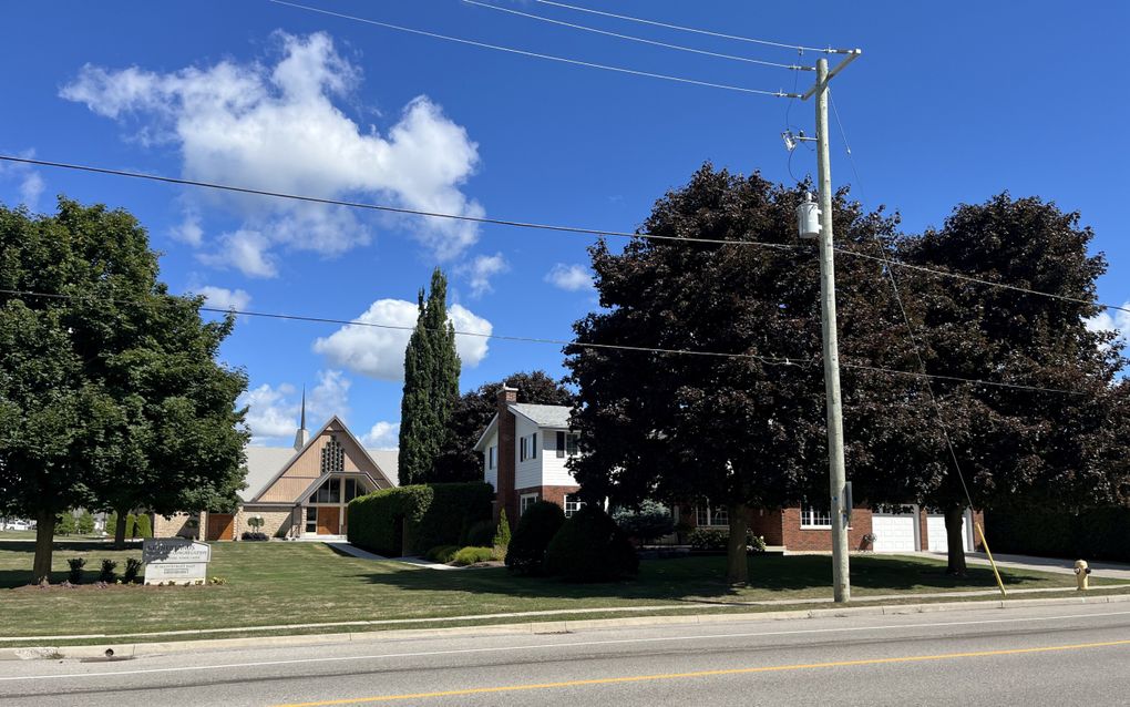 Groot Canadees jarenzestig kerkgebouw met een torentje, ervoor een woning tussen het groen.