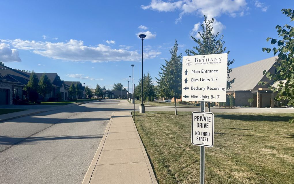 Bordje met bewegwijzering; erachter woningen en een kerk.