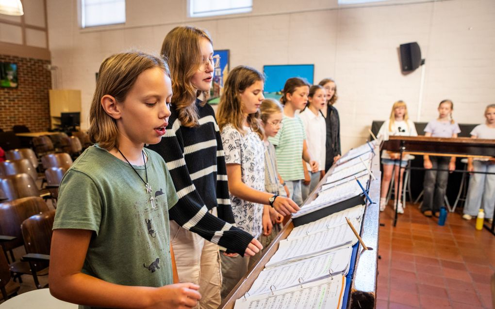 Zeven meiden staan achter lessenaars en zingen. Op de achtergrond zijn drie andere meiden te zien. 