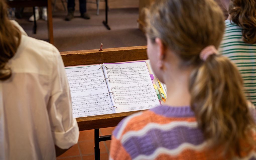 Detailfoto van een kind met een muziekstuk voor haar neus. Je kijkt over de schouder van het kind, dat een paardenstaart heeft, in de bladmuziek. 