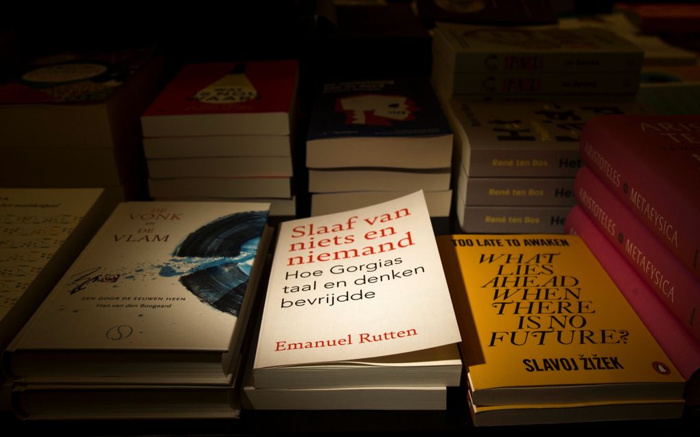Stapeltjes boeken. Het licht valt op het middelste stapeltje. Op de cover van het boek dat daarop ligt, staat: ”Slaaf van niets en niemand; hoe Gorgias taal en denken bevrijdde”, Emanuel Rutten.