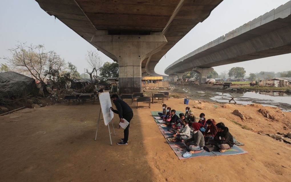 Leerlingen met mondkapjes zitten onder een brug terwijl ze les krijgen