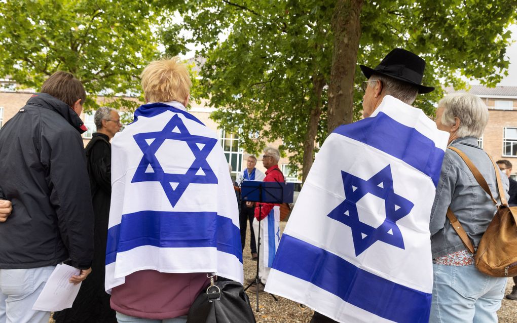 Vier mensen staan op een rij, op de rug gefotografeerd. Twee van hen hebben een Israëlische vlag omgeslagen.