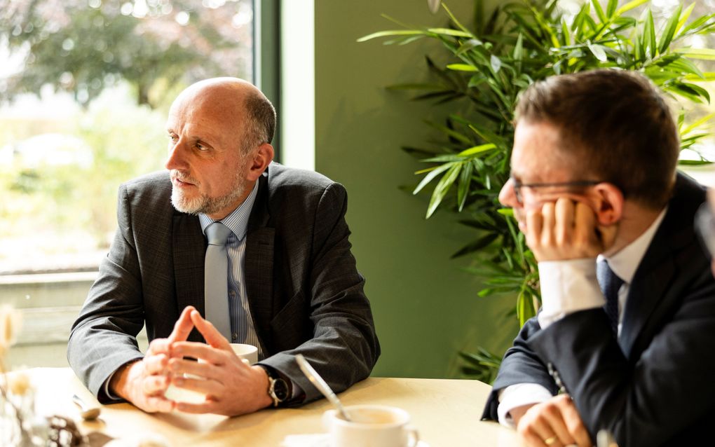 Twee mannen in donker pak, zittend aan een tafeltje.