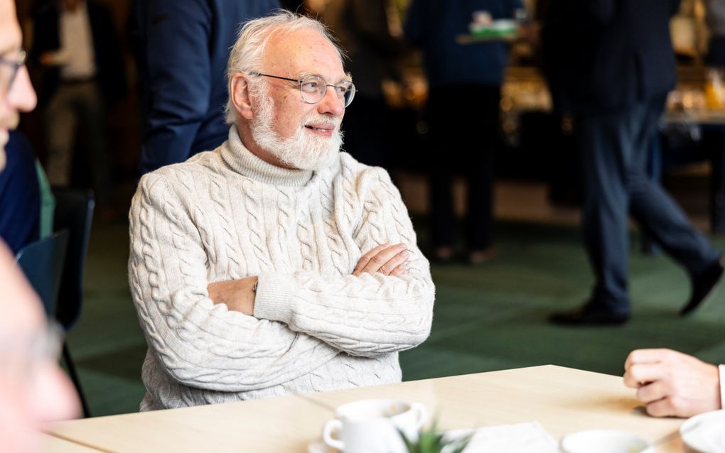 Man met witgrijze baard en bril, in witwollen kabeltrui, aan een tafeltje.