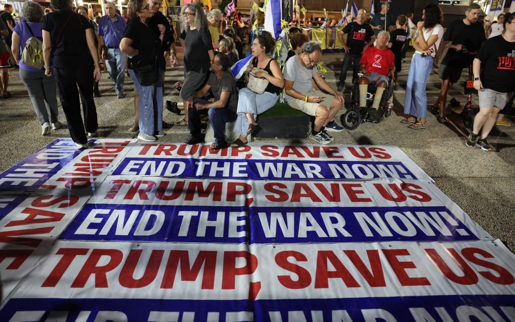 Een groot doek op de grond met opschrift ‘’Trump, save us, end the war now!’’ (diverse malen herhaald) met familieleden van de Israëlische gijzelaars erachter.