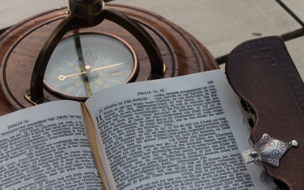 Opengeslagen Bijbel ligt bovenop kompas.
