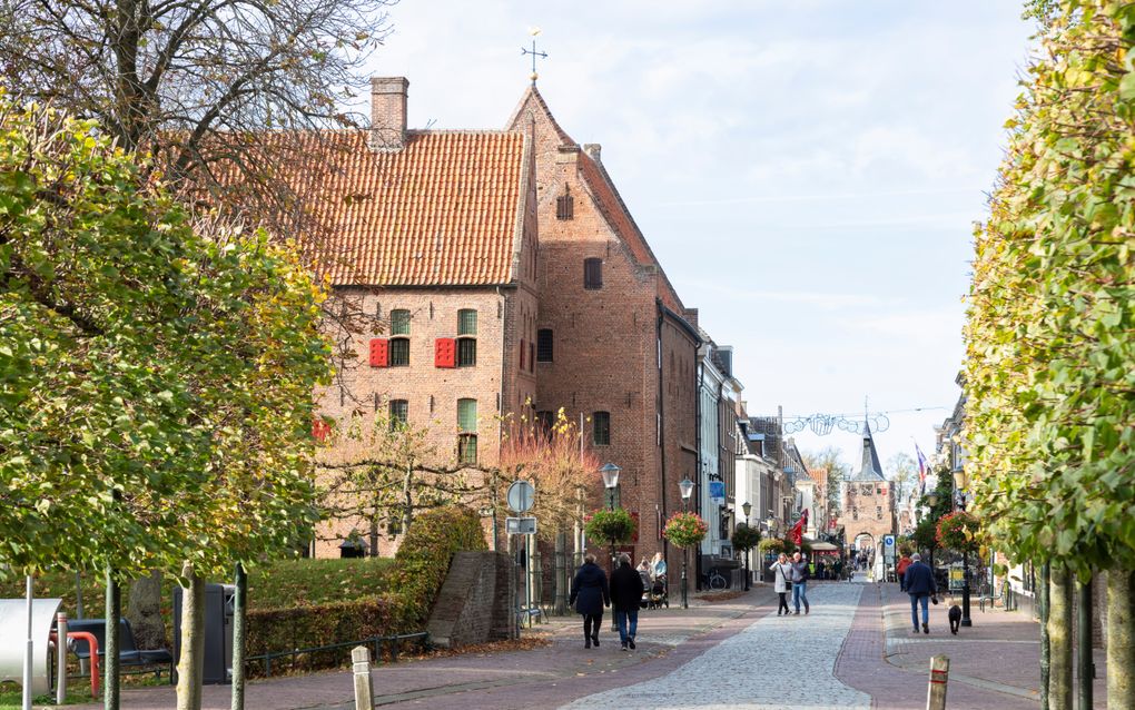 Historisch straatje waarin mensen lopen. Op de voorgrond herfstbomen, in de verte een stadspoort.