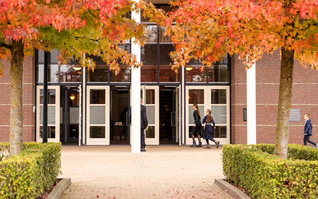 Kinderen lopen naar openstaande kerkdeuren met op de voorgrond bomen met herfstbladeren.