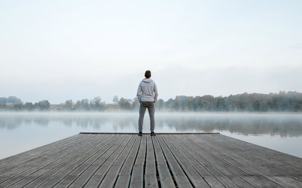 Jonge man staat aan het eind van een aanlegsteiger. Voor hem ligt een meer, met laaghangende mist.