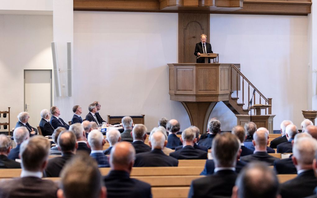 Een zittende groep mensen luistert vanuit kerkbanken naar een spreker op een houten kansel.