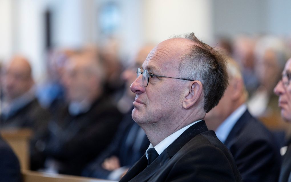 Een man in zwart pak zit op een kerkbank.