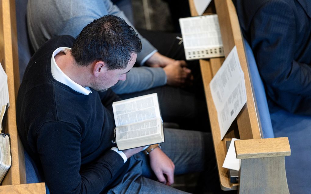 Een man in een kerkbank leest de Bijbel, die hij op schoot heeft.