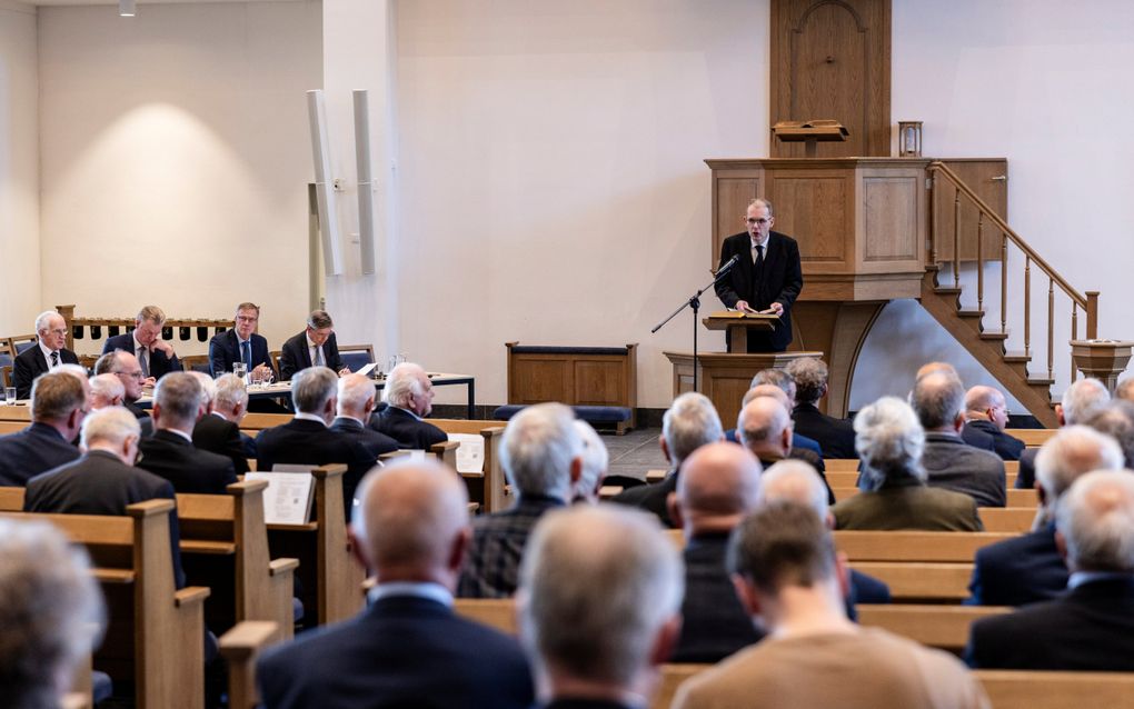 Een groep mensen zit op kerkbanken in een kerkzaal te luisteren naar een spreker.