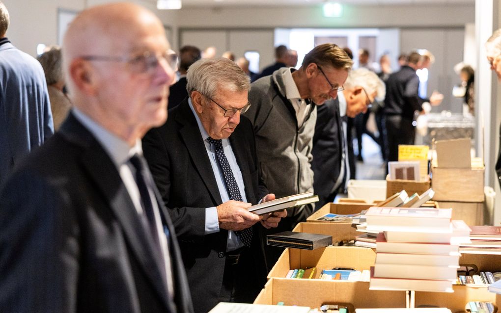 Enkele mannen staan gebogen over een boekentafel. Een van hen bekijkt een boekomslag.
