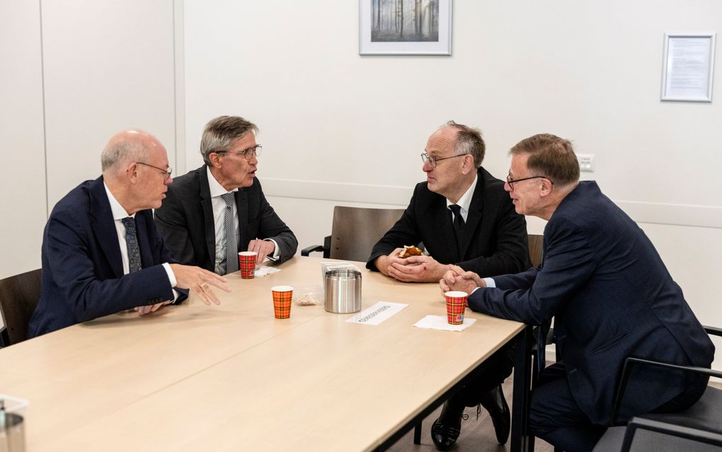 Aan tafel zitten vier mannen met elkaar te praten.