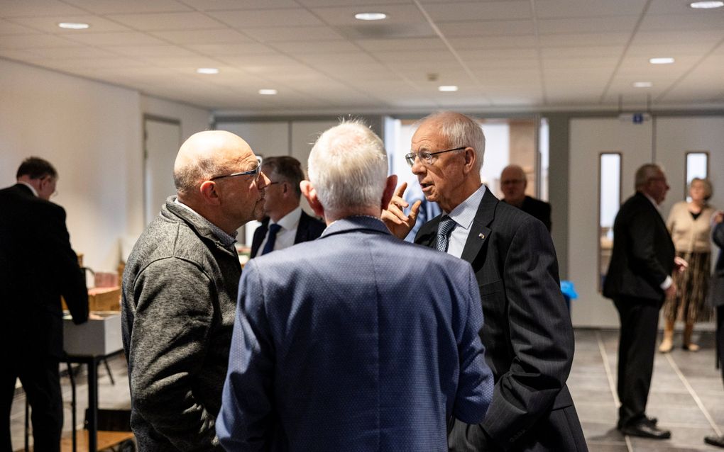 Drie mannen met grijs haar praten in een kerkhal met elkaar.