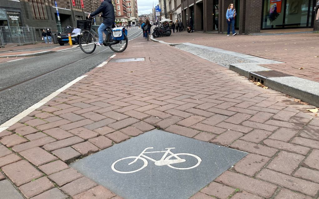 Vierkant tegel met daarop een witte fiets midden op het fietspad door Amsterdam.