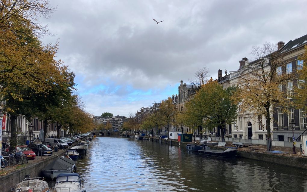 Amsterdamse gracht, met aan beide kades bootjes. In de verte een stenen boogbrug. Op de wal staan statige herenhuizen en bomen.