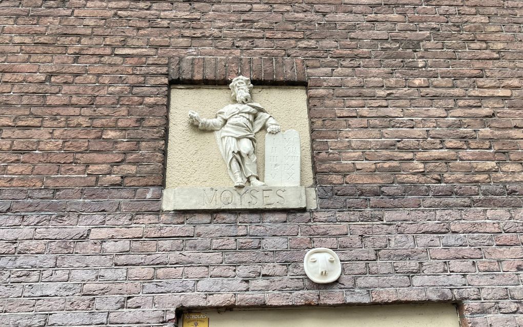 Gevelsteen, met daarop een mansfiguur. Hij leunt op een steen waar Hebreeuwse tekens in zijn gegraveerd. De figuur staat op een steen waar Moyses in staat te gebeiteld. 