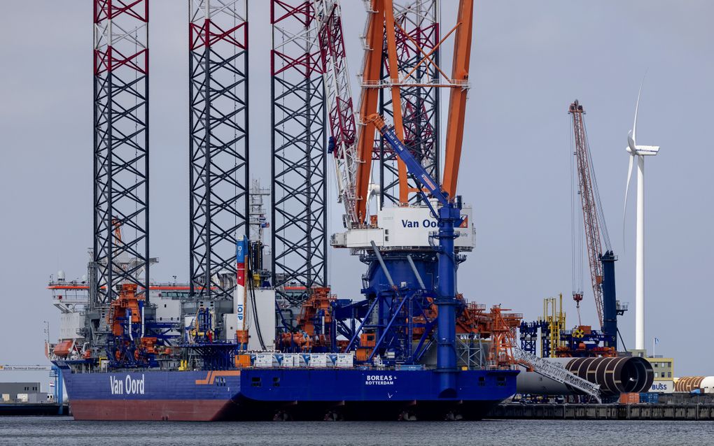 Een groot blauw schip met kranen erop ligt in een haven. Op het schip staat in grote letters de naam van het bedrijf Van Oord.