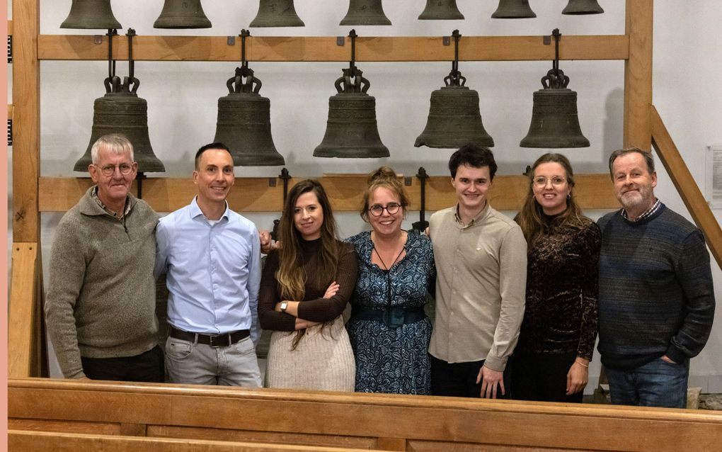 Een rij mensen, met op de achtergrond vijf kerkklokken.