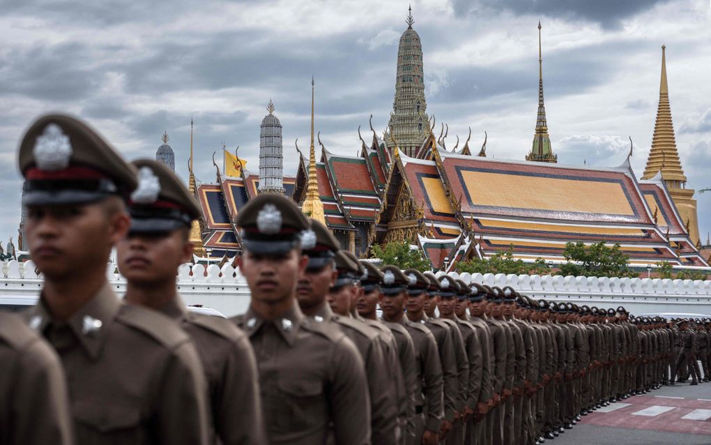 Politiemannen in donkere uniformen en met petten voor een paleis met veel goud