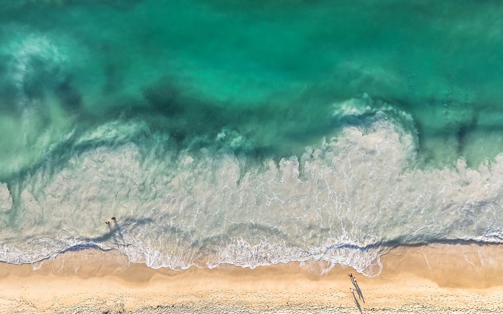 Luchtfoto van de zee, die bovenin groen is, en onderin wit van de golven
