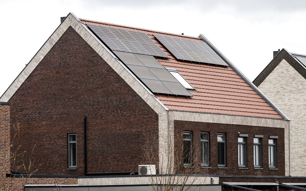 Zwarte zonnepanelen liggen op het dak van een woning met rode dakpannen.