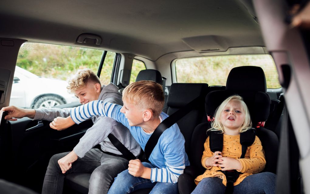 Twee jongens zitten te stoeien met elkaar op de achterbank van een auto.
