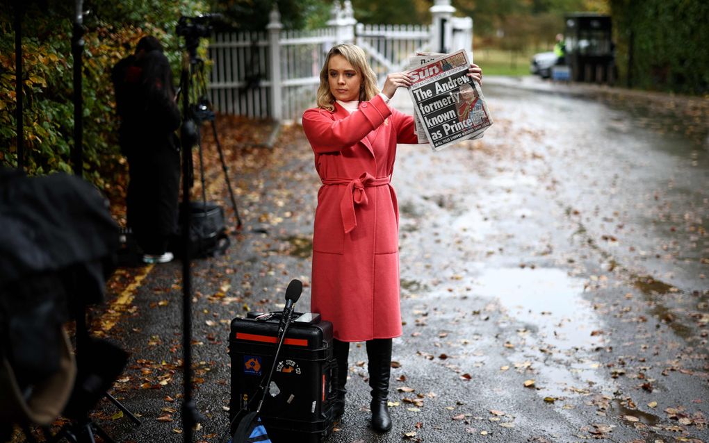 Een vrouw in een rode jas houdt in de regen een krant omhoog. 