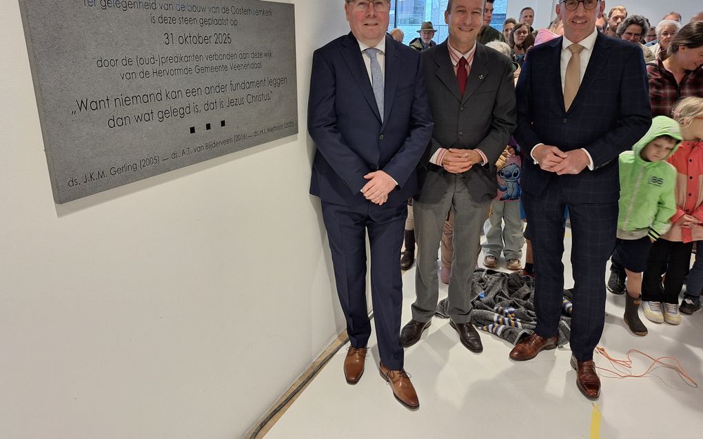 Drie mannen in pak, achter hen gezinnen met kinderen.