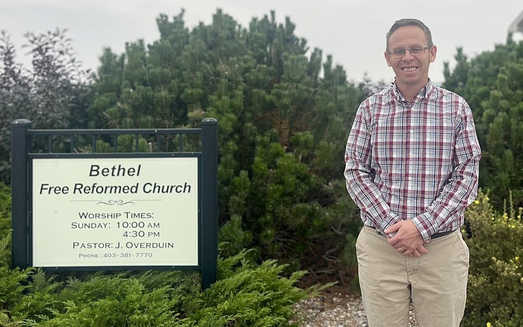 Man met geruit overhemd en lichte broek staat voor een bossage.