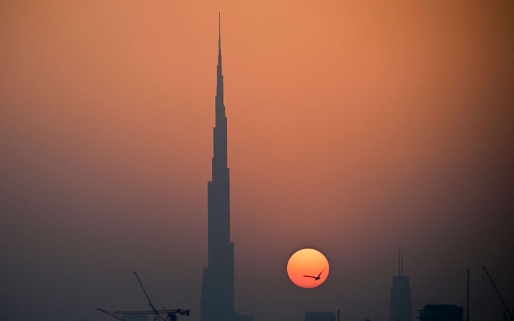 Een hoog gebouw met een punt. Naast het gebouw is de zon te zien. 